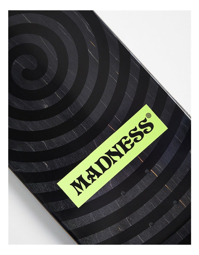 Close-up of a skateboard deck showing a black wood grain spiral pattern and a bright neon yellow-green sticker with the brand name 'MADNESS' in black.