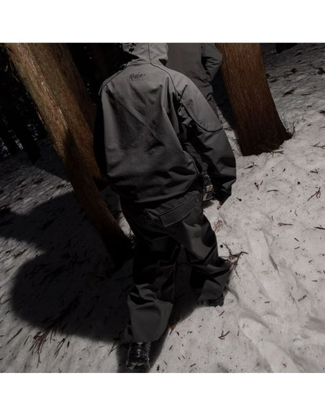 Person wearing a dark jacket and pants standing in a snowy landscape with trees.