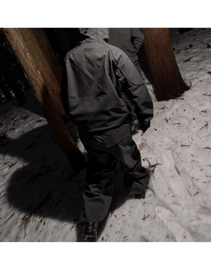 Person wearing a dark jacket and pants standing in a snowy landscape with trees.
