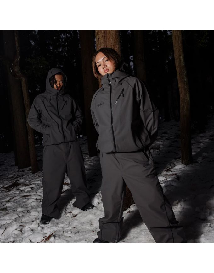 Two people wearing matching gray outfits standing in a snowy forest.