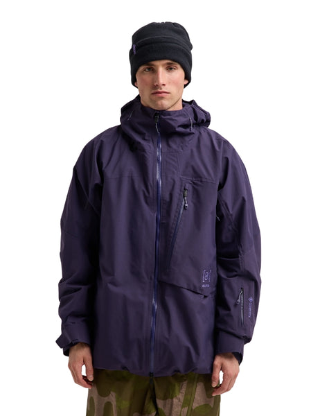 A man wearing a dark purple Arc'teryx hooded jacket, a black beanie, and camouflage pants, standing against a solid white background.