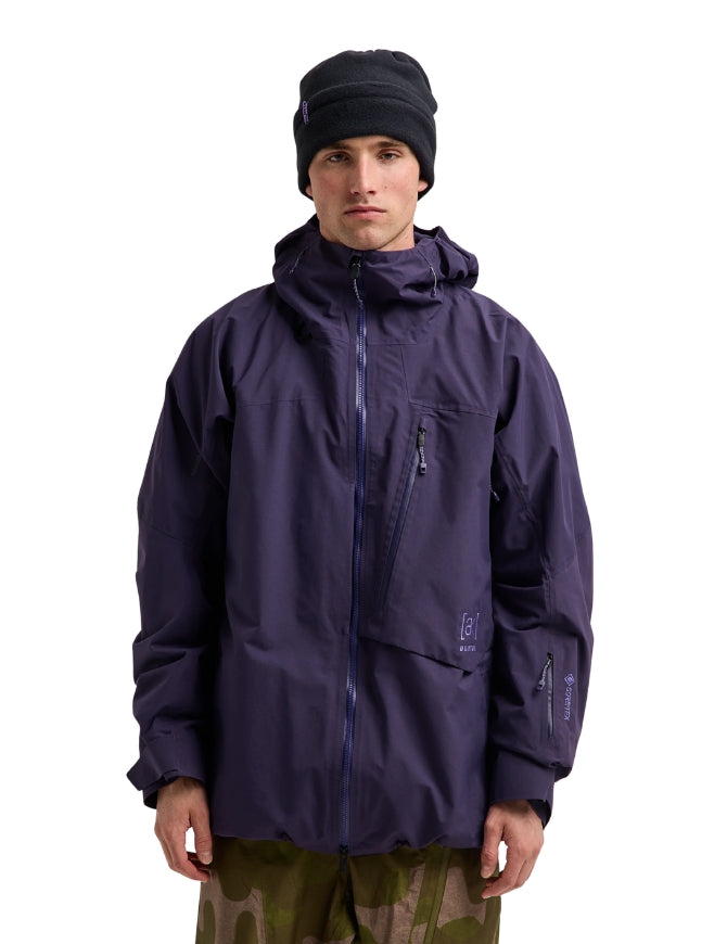 A man wearing a dark purple Arc'teryx hooded jacket, a black beanie, and camouflage pants, standing against a solid white background.