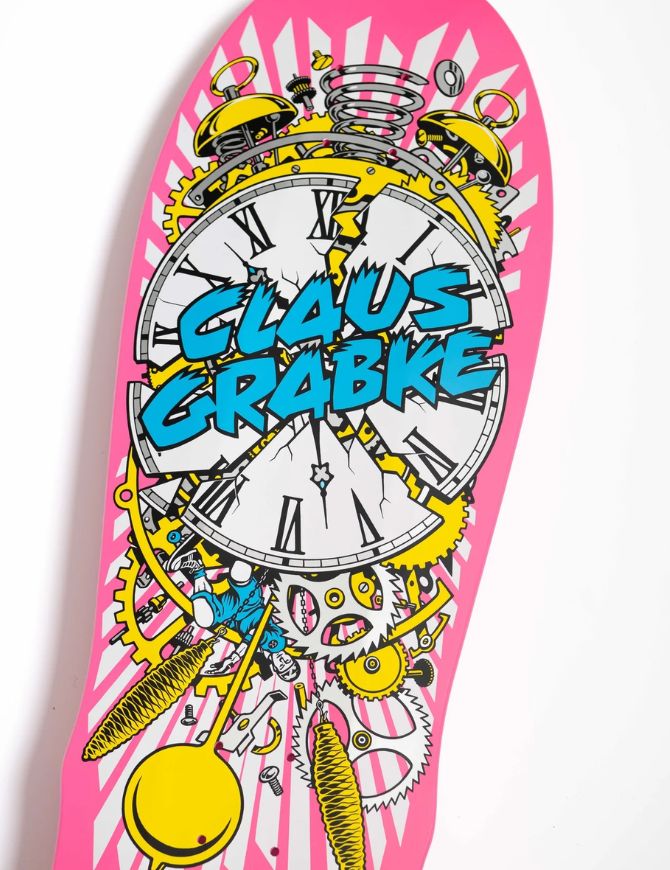 A pink skateboard deck featuring a whimsical steampunk design with a large clock face, gears, springs, and the text 'CLAUS GRABKE' in bold blue letters, shown against a plain white background.
