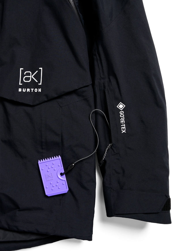 Close-up of a black Burton jacket with a purple branded hangtag, showing the Burton logo on the chest and a Gore-Tex label on the sleeve, against a white background.