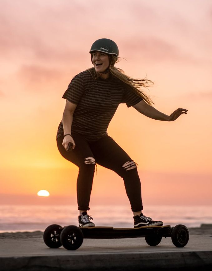 Person riding a longboard on a beach at sunset