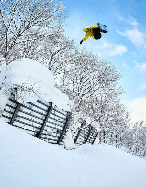 Person snowboarding off a jump with snowy landscape and trees in the background