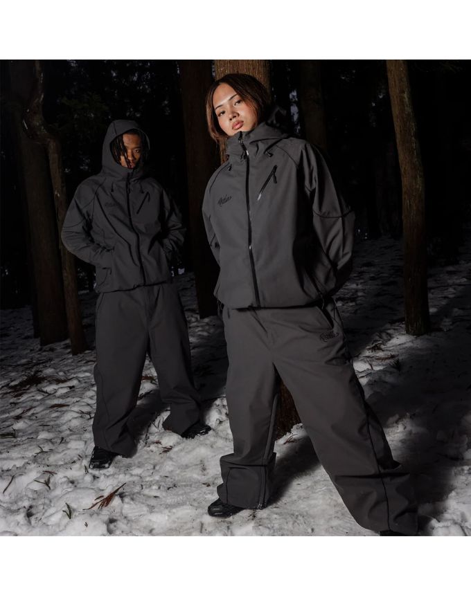 Two people wearing gray winter suits standing in a snowy forest.