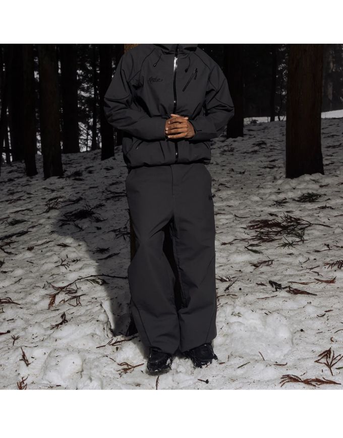Person wearing a dark gray snowsuit standing in a snowy forest.