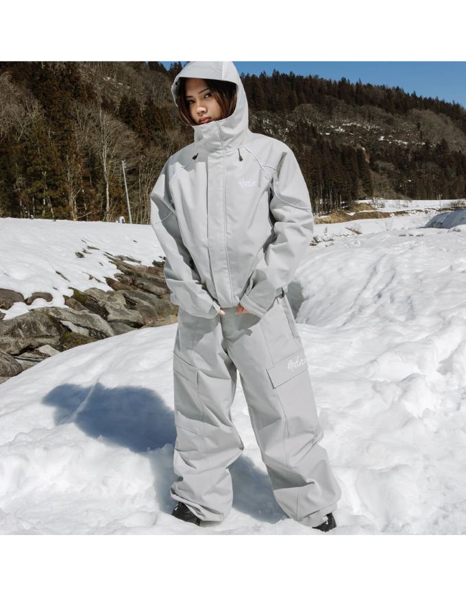 Person wearing a light gray snowsuit standing in a snowy landscape with trees in the background.