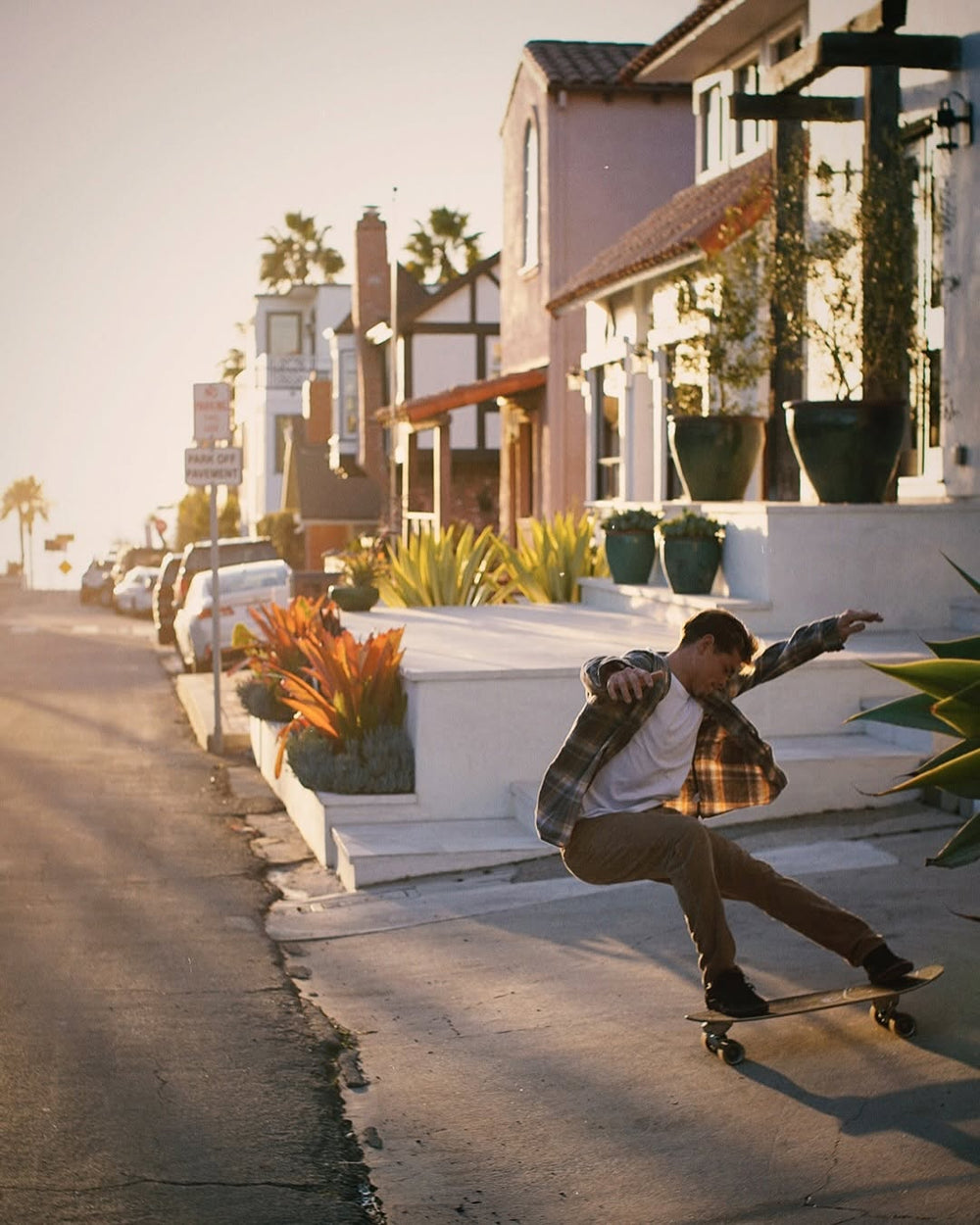 Person skateboarding on a sidewalk with residential buildings and palm trees in the background